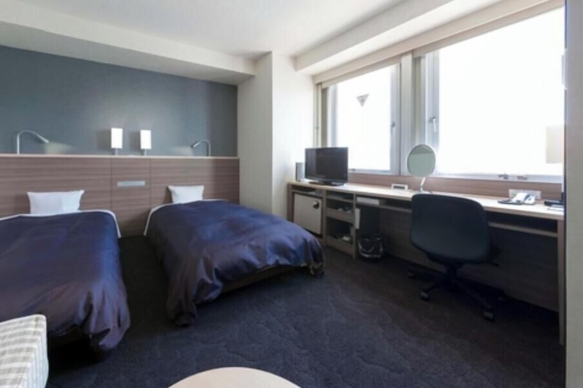 Une chambre d’hôtel avec deux lits, un bureau avec un ordinateur, une chaise et une fenêtre.