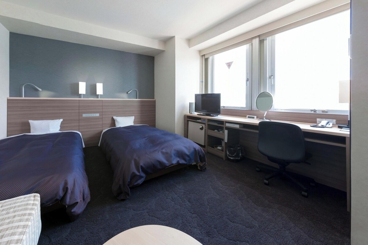 Une chambre d’hôtel avec deux lits, un bureau avec un ordinateur, une télévision et une fenêtre.