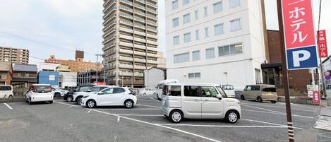 A parking lot with multiple cars, a white van, and a building with a red sign in the background.