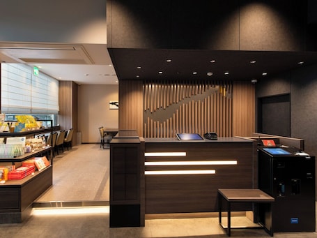 A modern reception desk with a wooden finish, a staircase, and a seating area with chairs.
