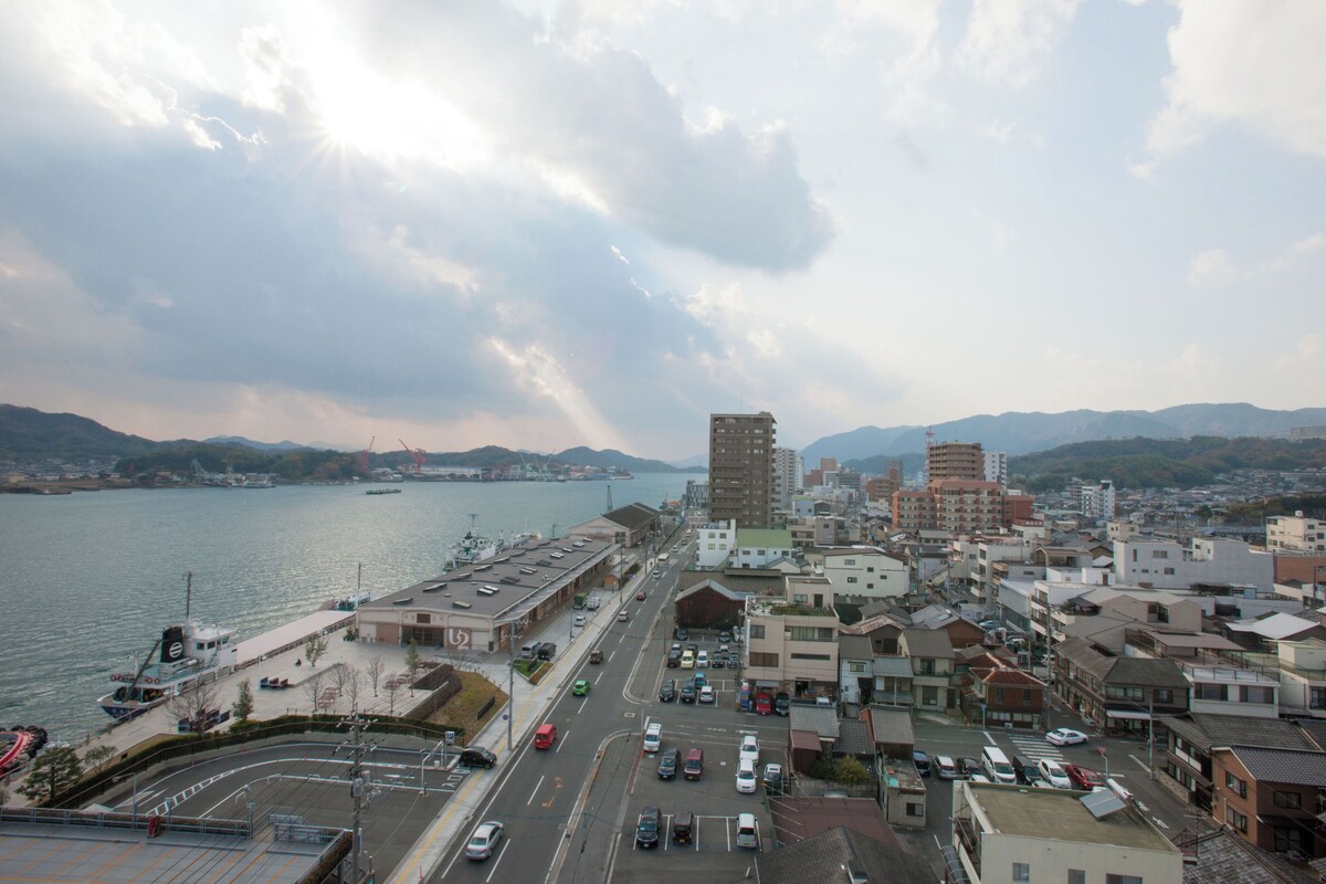 Un paysage urbain côtier avec un port de plaisance, des bâtiments et un pont au loin.