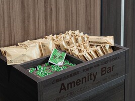 A wooden crate labeled 'Amenity Bar' with various packaged items, including a green packet and several brown paper bags.