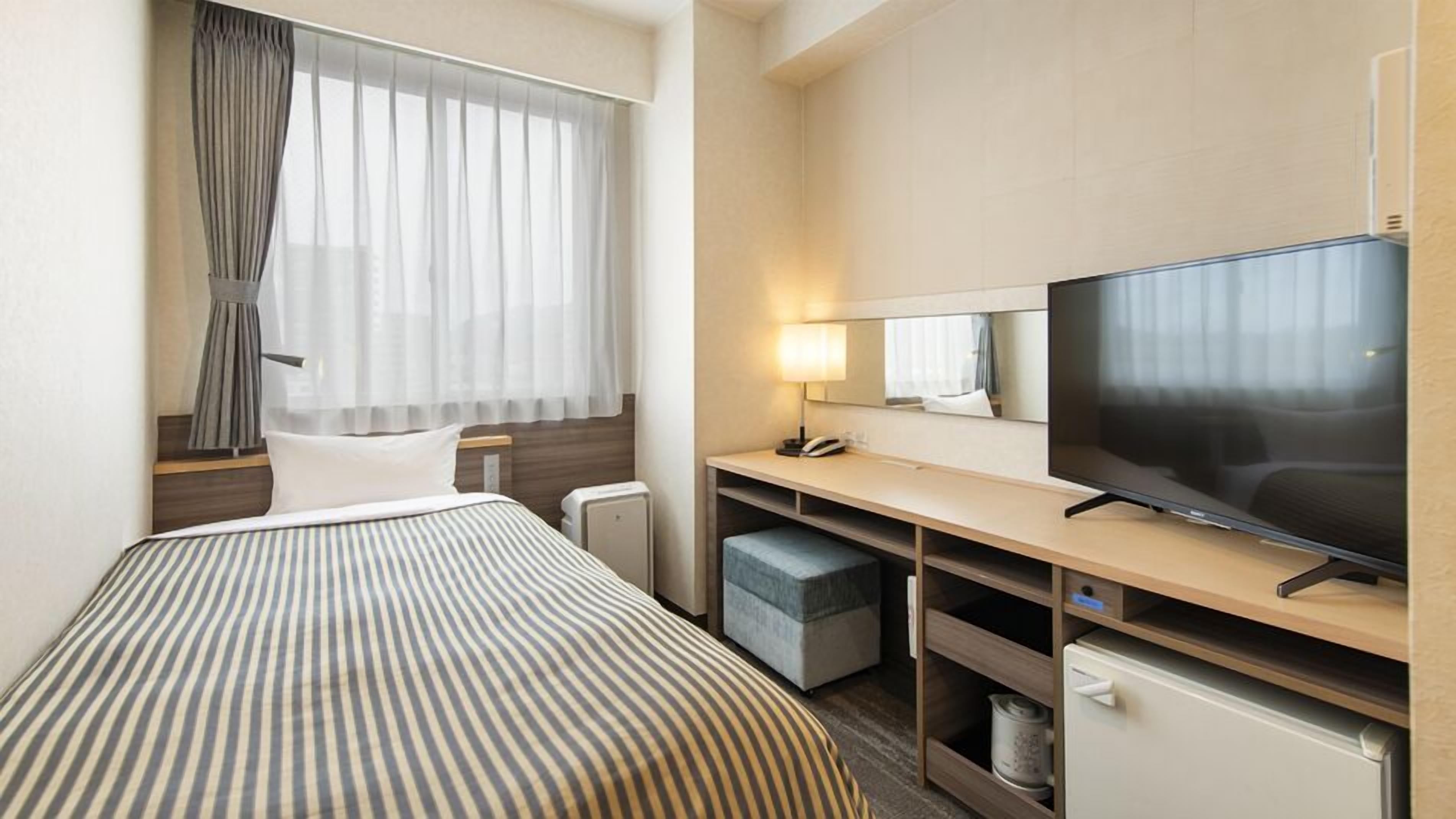 Una habitación de hotel con cama, escritorio, televisor, espejo y ventana con cortinas.