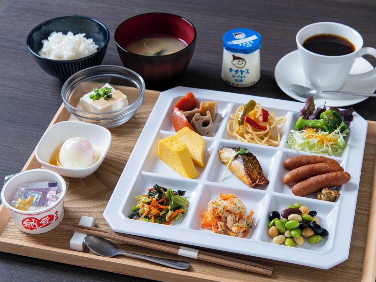 Bandeja de comida con diversos platos, incluyendo tofu, fideos, verduras y una taza de café.