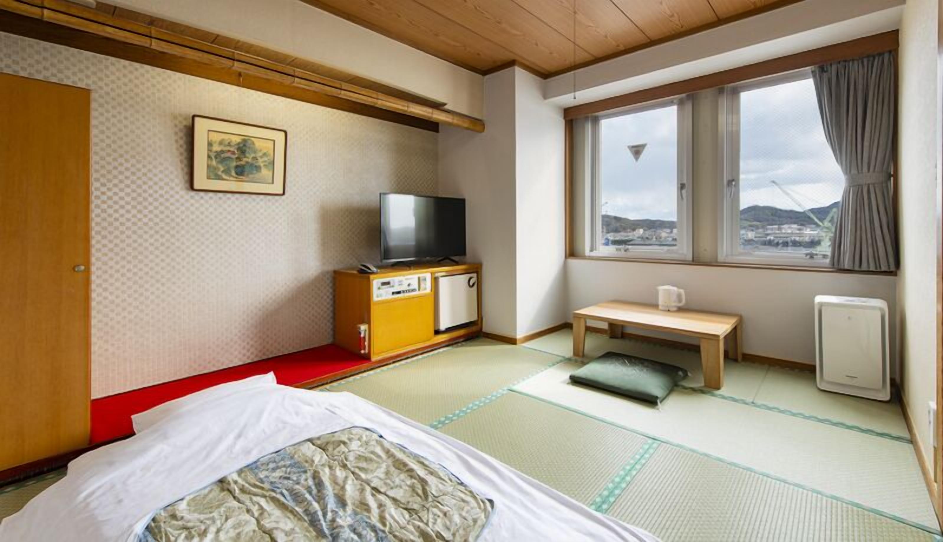 Una habitación japonesa tradicional con suelo de tatami, un futón, un televisor, un mueble bajo y una ventana con vistas, además de un calentador.