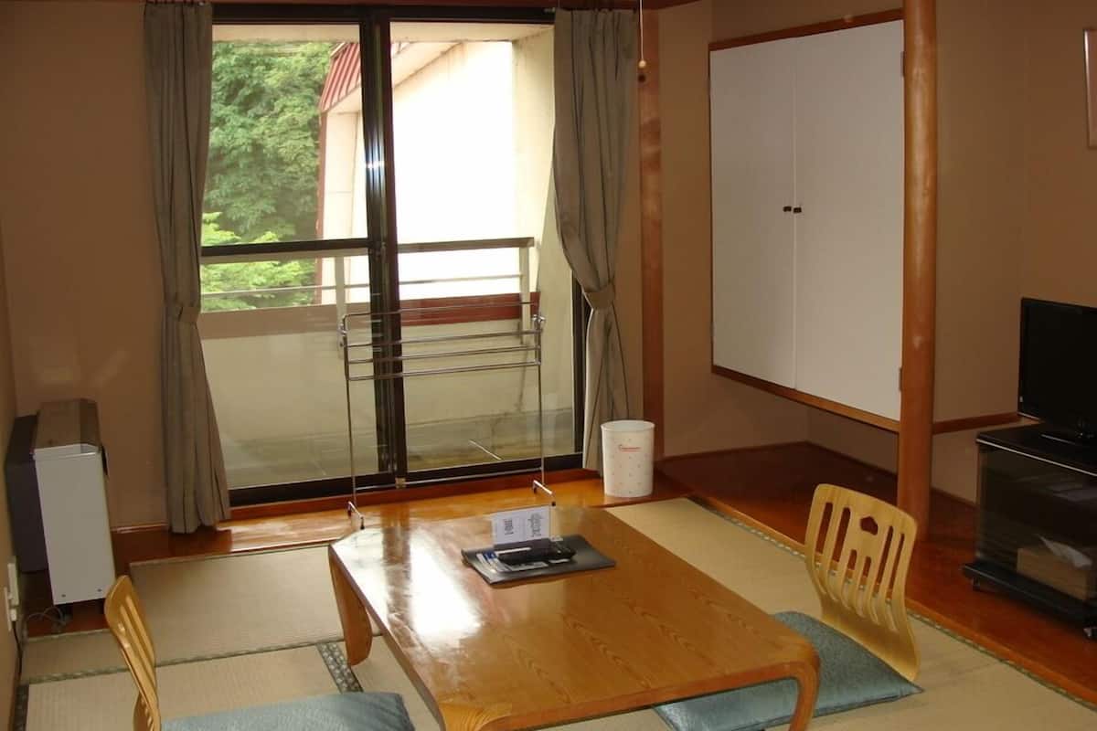 A room with a sliding glass door leading to a balcony, a wooden table with a chair, a television, and a cabinet.