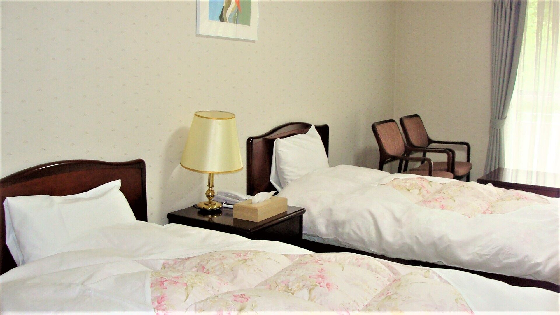 Una habitación de hotel con dos camas, una mesita de noche con lámpara, una silla y una pequeña mesa.