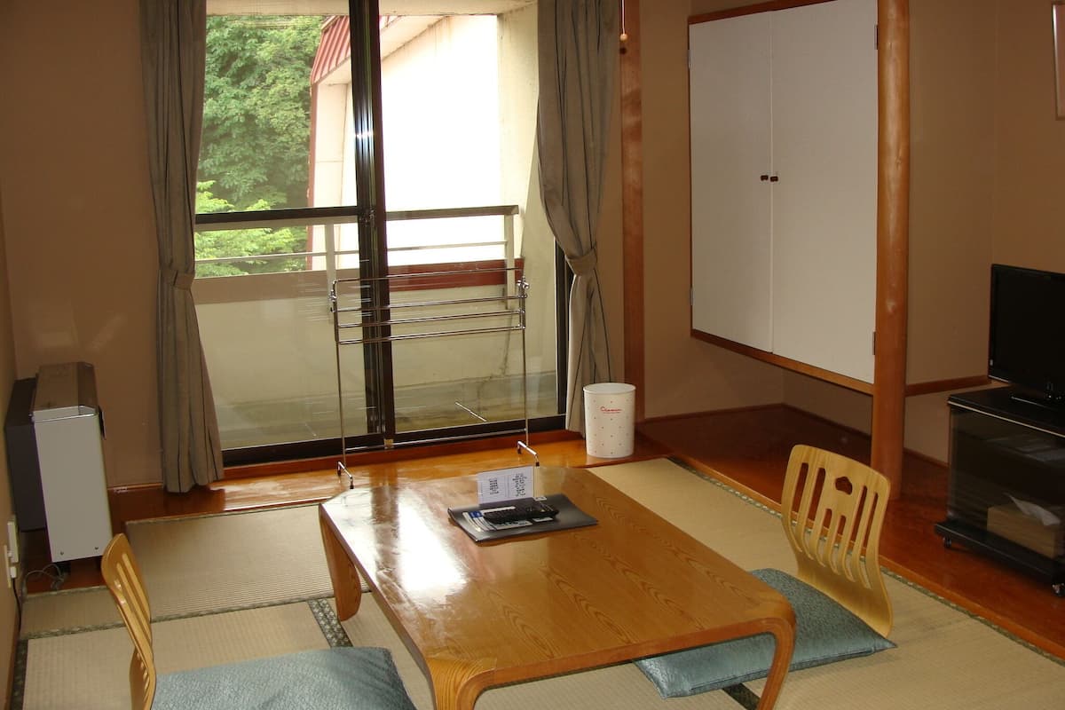 A room with a sliding glass door leading to a balcony, a wooden table with a chair, a television, and a cabinet.