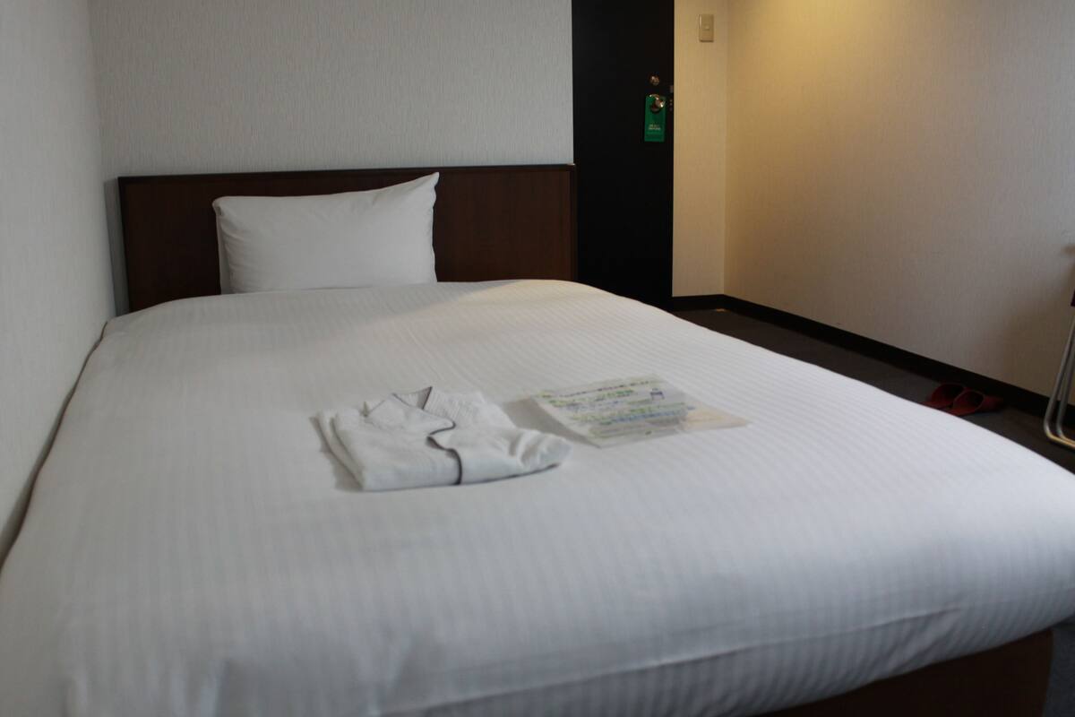 A neatly made bed with white linens, a folded towel, and a magazine on the bed.