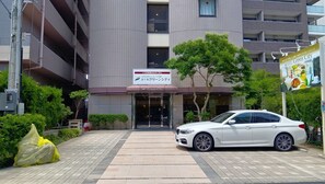 Entrada de hotel con un coche estacionado frente a ella, un cartel y un edificio de varios pisos.