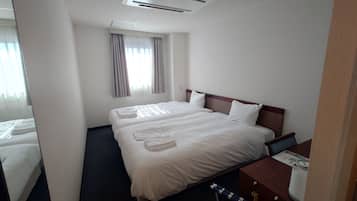 A hotel room with a double bed, a bedside table, a window with curtains, and a small desk with a chair.