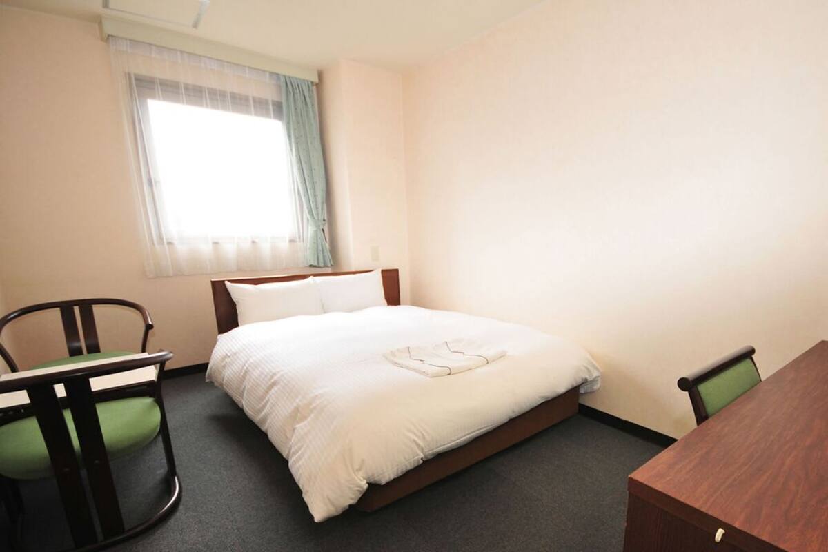 A hotel room with a bed, a desk with a computer, and two chairs.