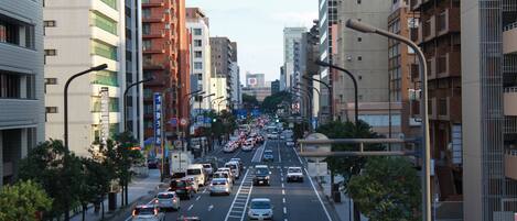 Una calle urbana concurrida flanqueada por edificios de varios pisos, tráfico y farolas.