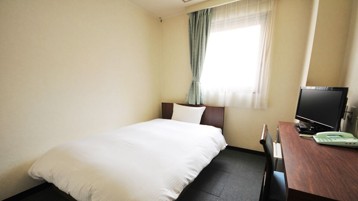 Ein Hotelzimmer mit einem Bett, einem Schreibtisch mit Fernseher und einem Fenster mit Vorhängen.