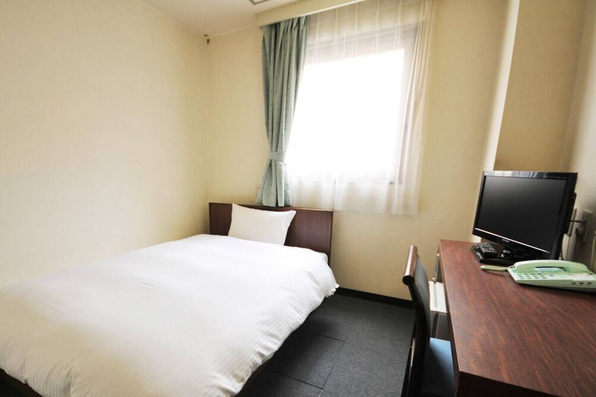 A hotel room with a bed, a desk with a TV, and a window with curtains.