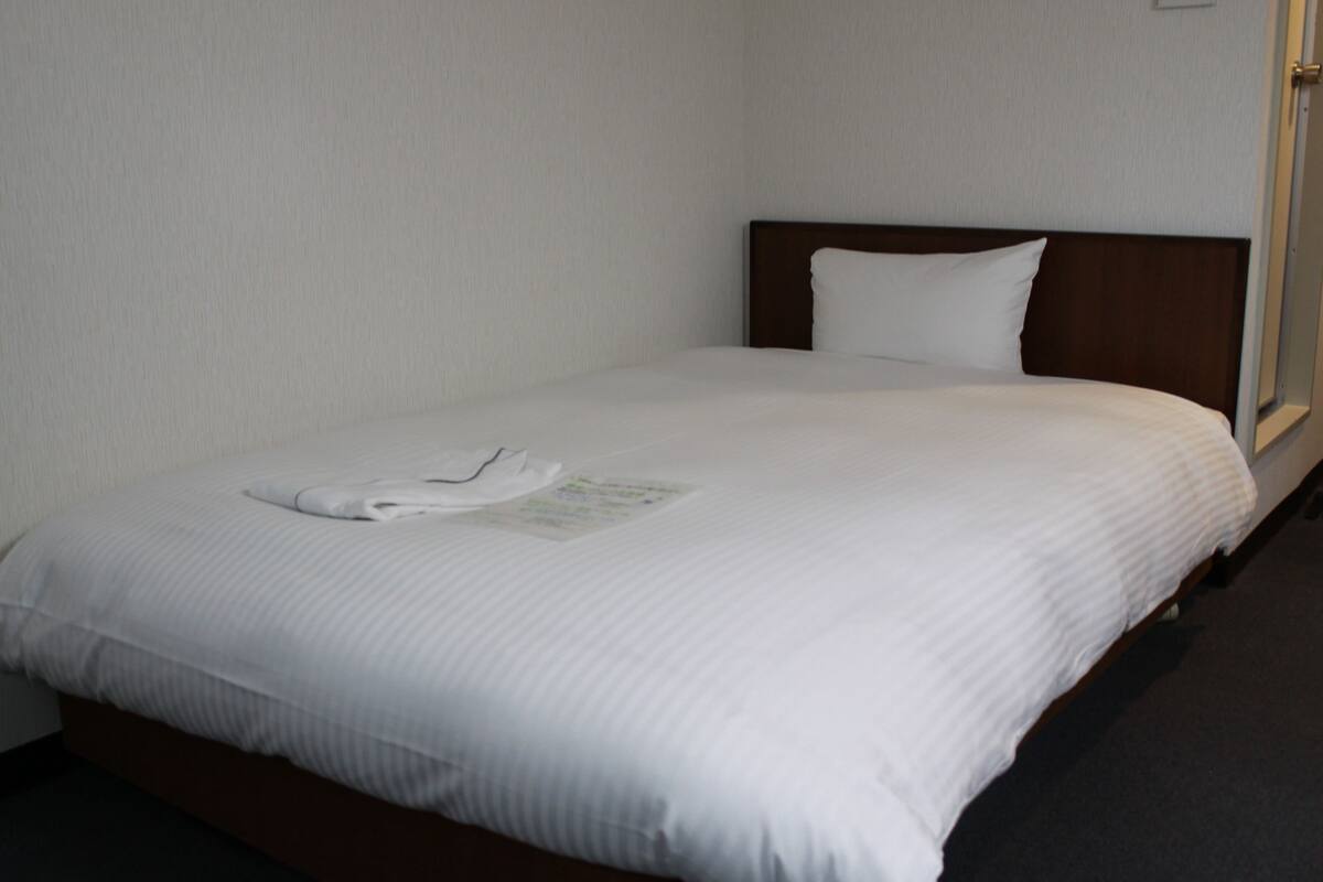 A neatly made bed with a white comforter and pillows, a folded white towel, and a small informational card on the bed.
