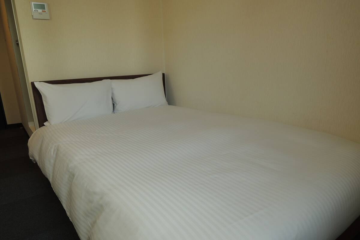 A hotel room with a large bed, a headboard, and a thermostat on the wall.