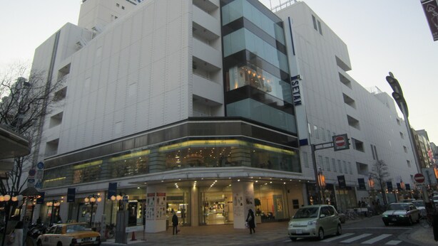 A modern building with a glass facade, multiple floors, and a prominent sign on the top. - Hotel Dorf Shizuoka (Shizuoka)