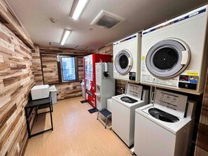 A laundry room with multiple washing machines, a vending machine, and a small table. - Hotel New Saitama (Saitama)