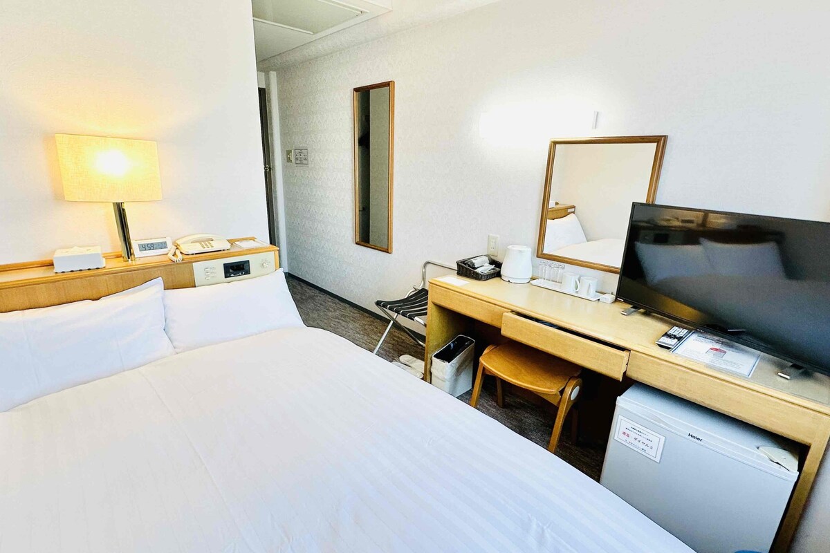 A hotel room with a bed, desk, TV, and a small refrigerator.
