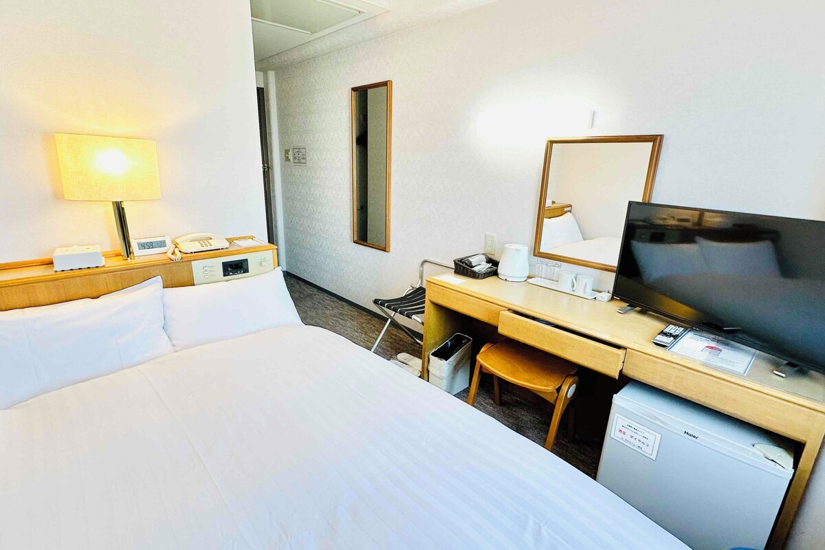 A hotel room with a bed, desk, TV, and a small refrigerator.
