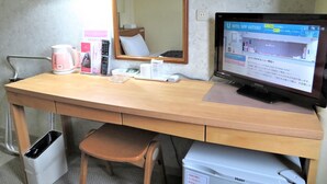 Mesa de quarto de hotel com um computador, uma cafeteira, um controle remoto e um espelho.
