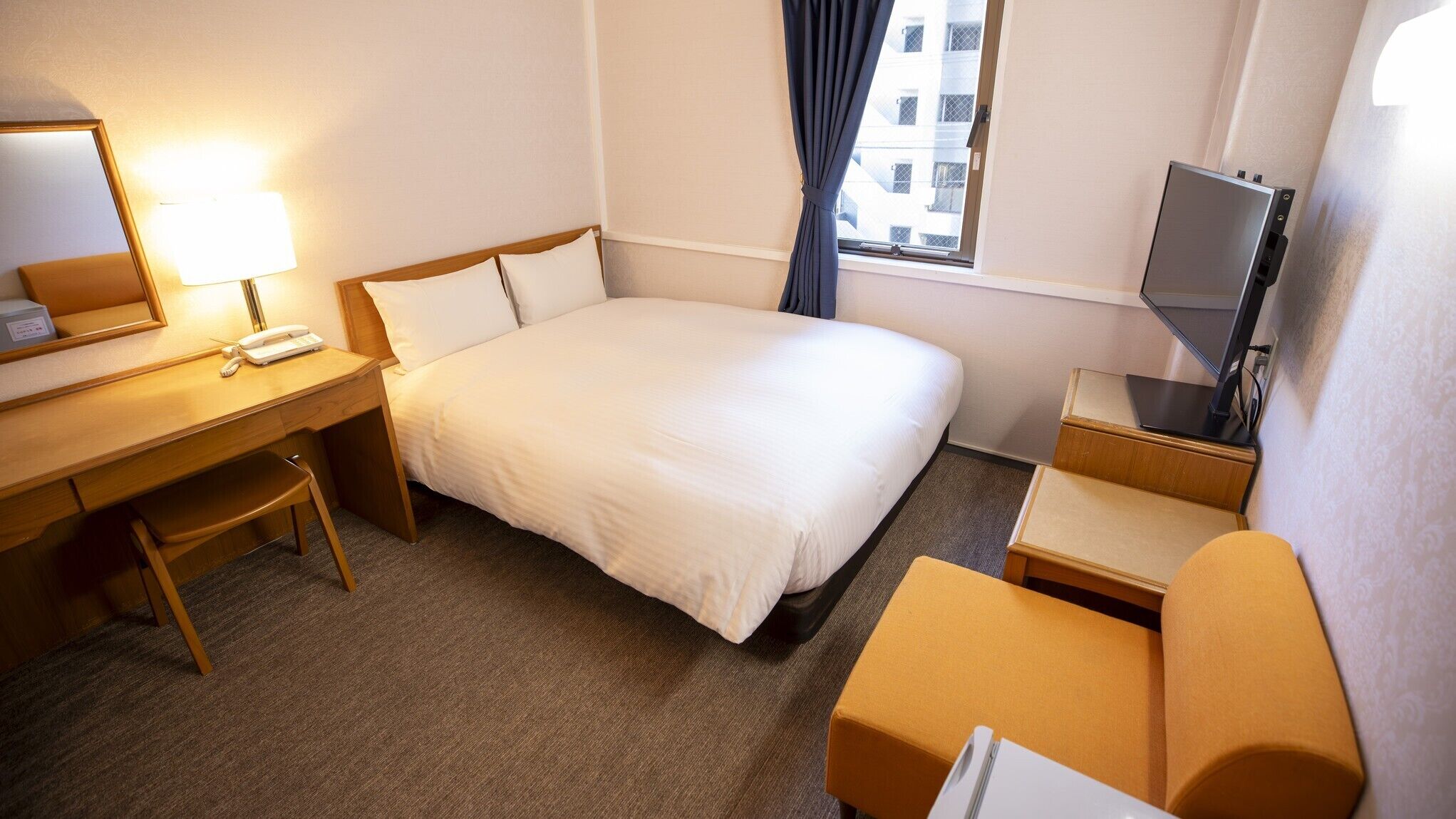 Une chambre d’hôtel équipée d’un lit, d’un bureau, d’une chaise, d’une télévision et d’une fenêtre avec des rideaux.