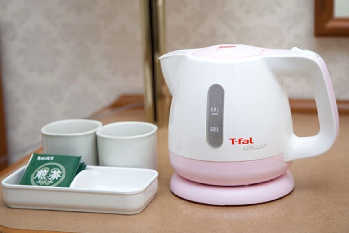 A white and pink electric kettle with a digital display, a tray with two white cups and a green tea packet, and a wooden table.