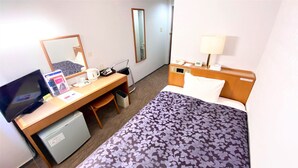 Quarto de hotel com cama, escrivaninha com computador, televisão, espelho, abajur e pequeno frigorífico.