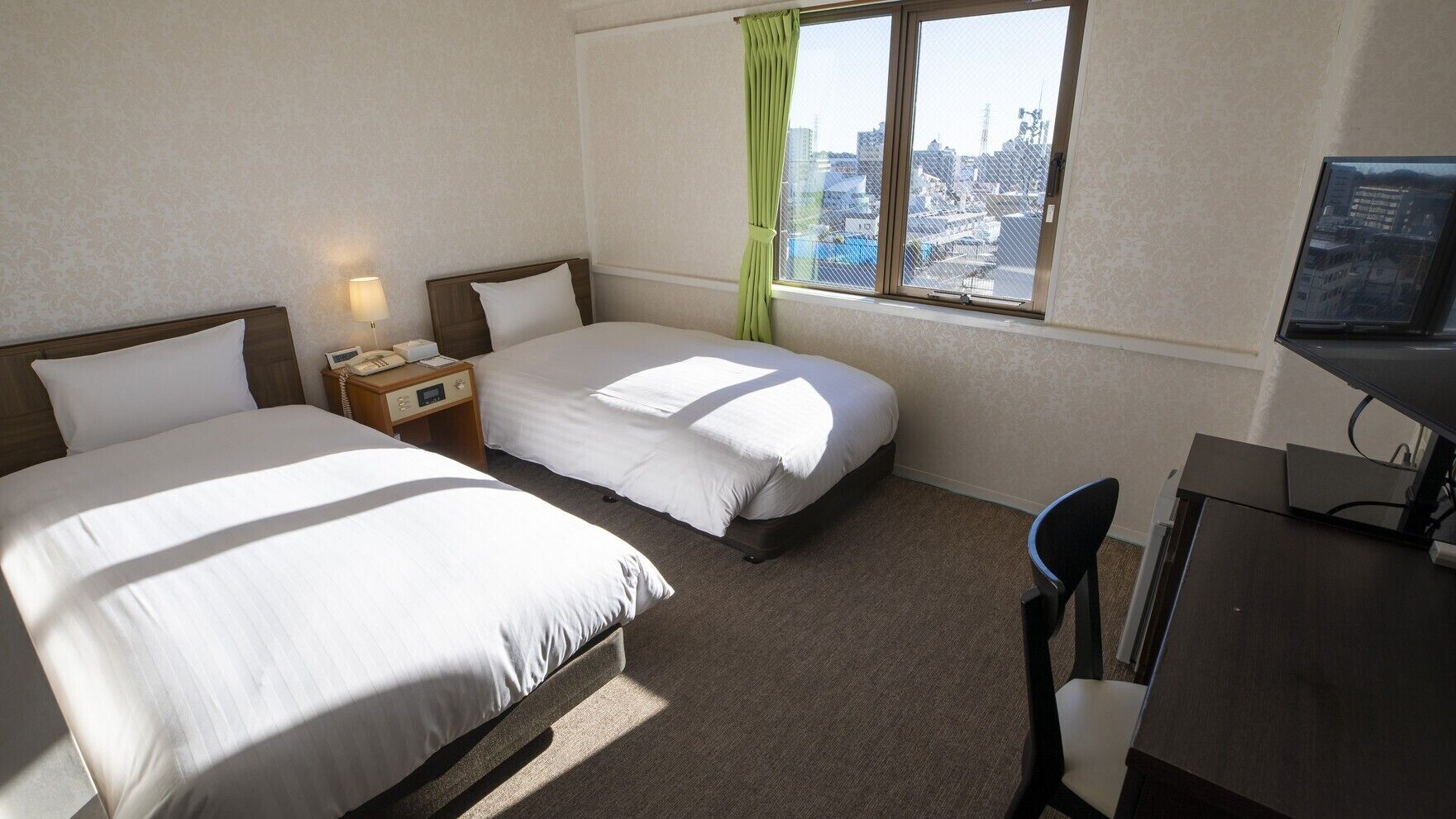 Une chambre d’hôtel avec deux lits, un bureau, une chaise, une télévision et une fenêtre donnant sur la ville.