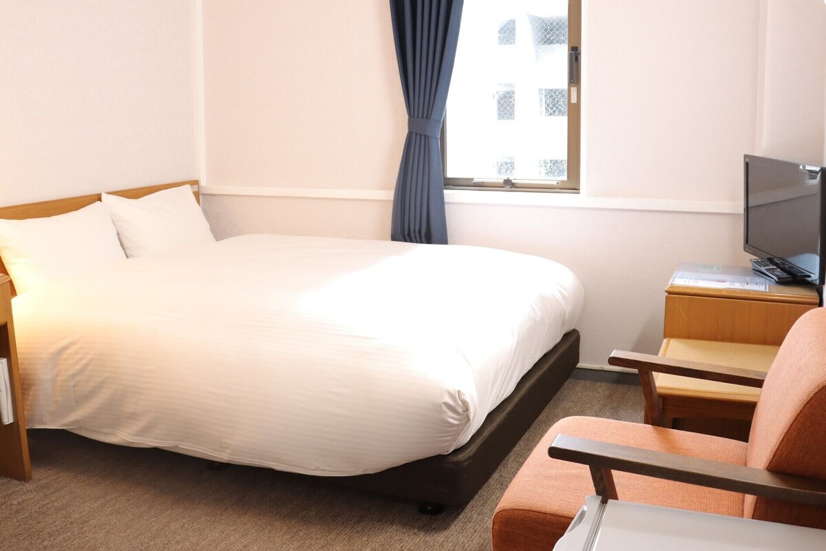 A hotel room with a bed, a desk with a computer, a chair, and a TV.