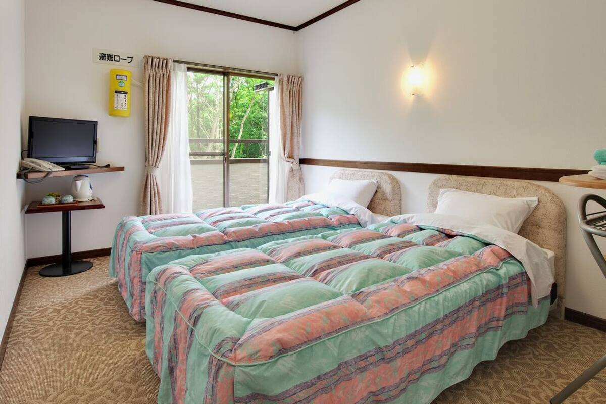 A hotel room with two beds, a television, a desk with a telephone, and a window with curtains.