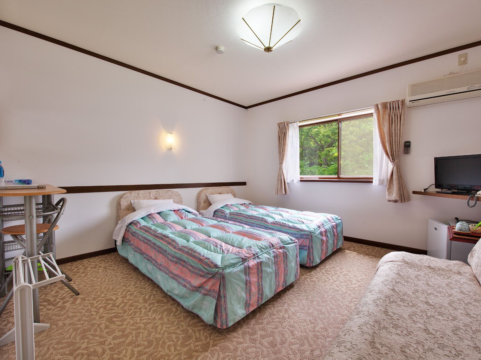 A hotel room with two beds, a desk with a chair, a television, and a window with curtains.