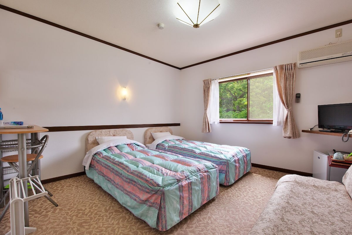 A hotel room with two beds, a desk with a chair, a television, and a window with curtains.