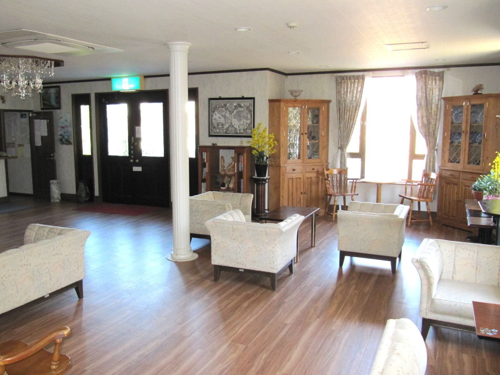 A spacious lobby with a wooden floor, several sofas, a chandelier, and a large window with curtains.