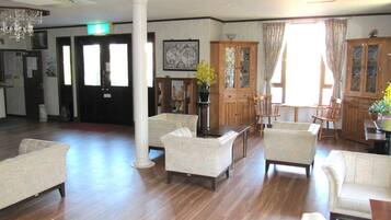A spacious lobby with a wooden floor, several sofas, a chandelier, and a large window with curtains.
