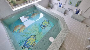 A bathroom with a mosaic pool, a window with a view of greenery, and a sink with toiletries. - Château Le Fleur (Ito)