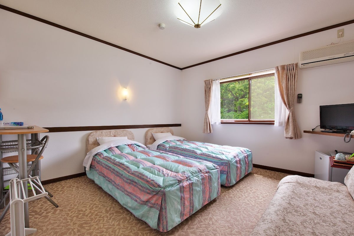 A hotel room with two beds, a desk with a chair, a television, and a window with curtains.