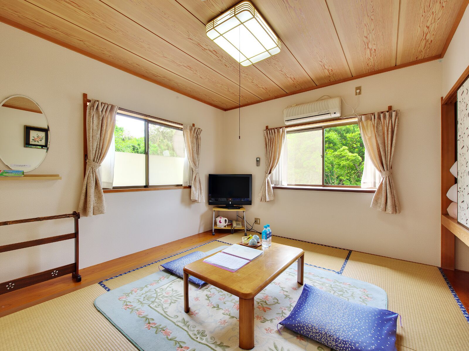 A room with tatami flooring, a wooden table, a television, and two windows with curtains.