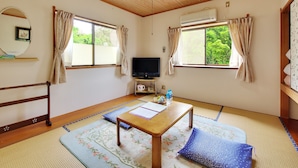 A traditional Japanese room with tatami flooring, a wooden table, a television, and a view of greenery outside. - Château Le Fleur (Ito)