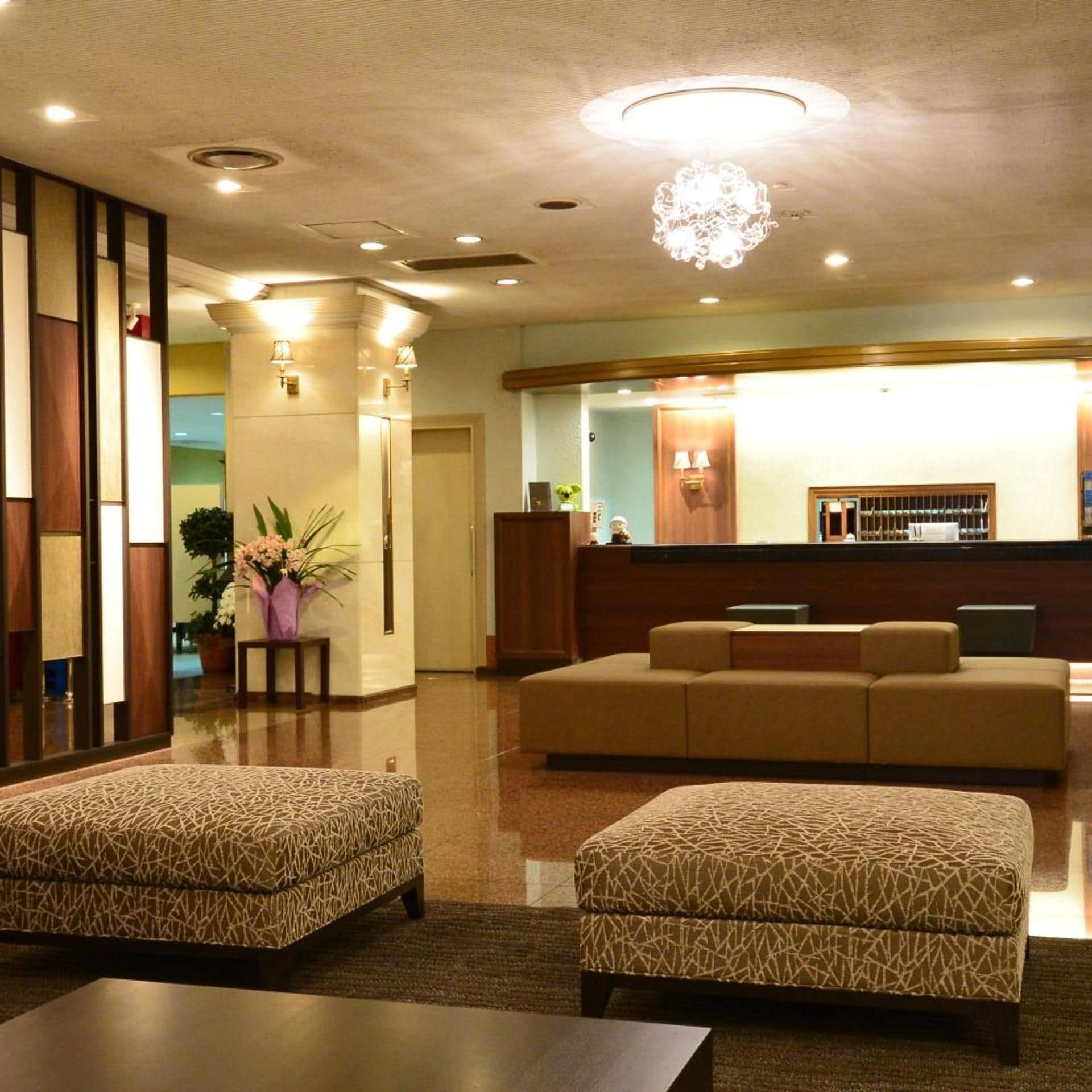 Eine Hotelhalle mit einer Rezeption, einer Sitzecke und einem dekorativen Kronleuchter.