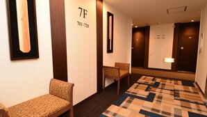 A hotel hallway with a checkered carpet, a wooden bench, a wall-mounted bat, and a door with room numbers. - Hotel Sunroute Sano (Sano)
