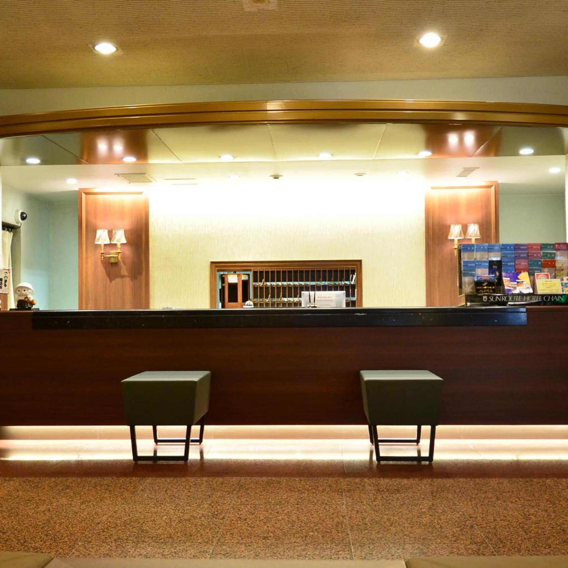 A reception area with a wooden reception desk, two chairs, and a counter displaying a SunRoute Hotel Chain sign.