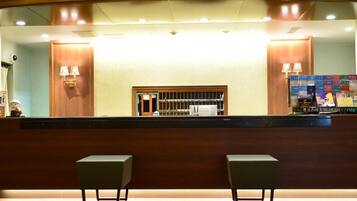 A reception area with a wooden reception desk, two chairs, and a counter displaying a SunRoute Hotel Chain sign.