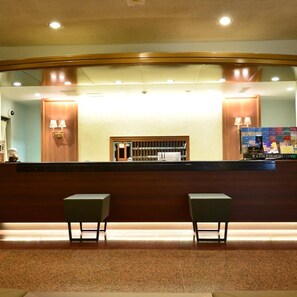 A reception area with a wooden reception desk, two chairs, and a counter displaying a SunRoute Hotel Chain sign. - Hotel Sunroute Sano (Sano)
