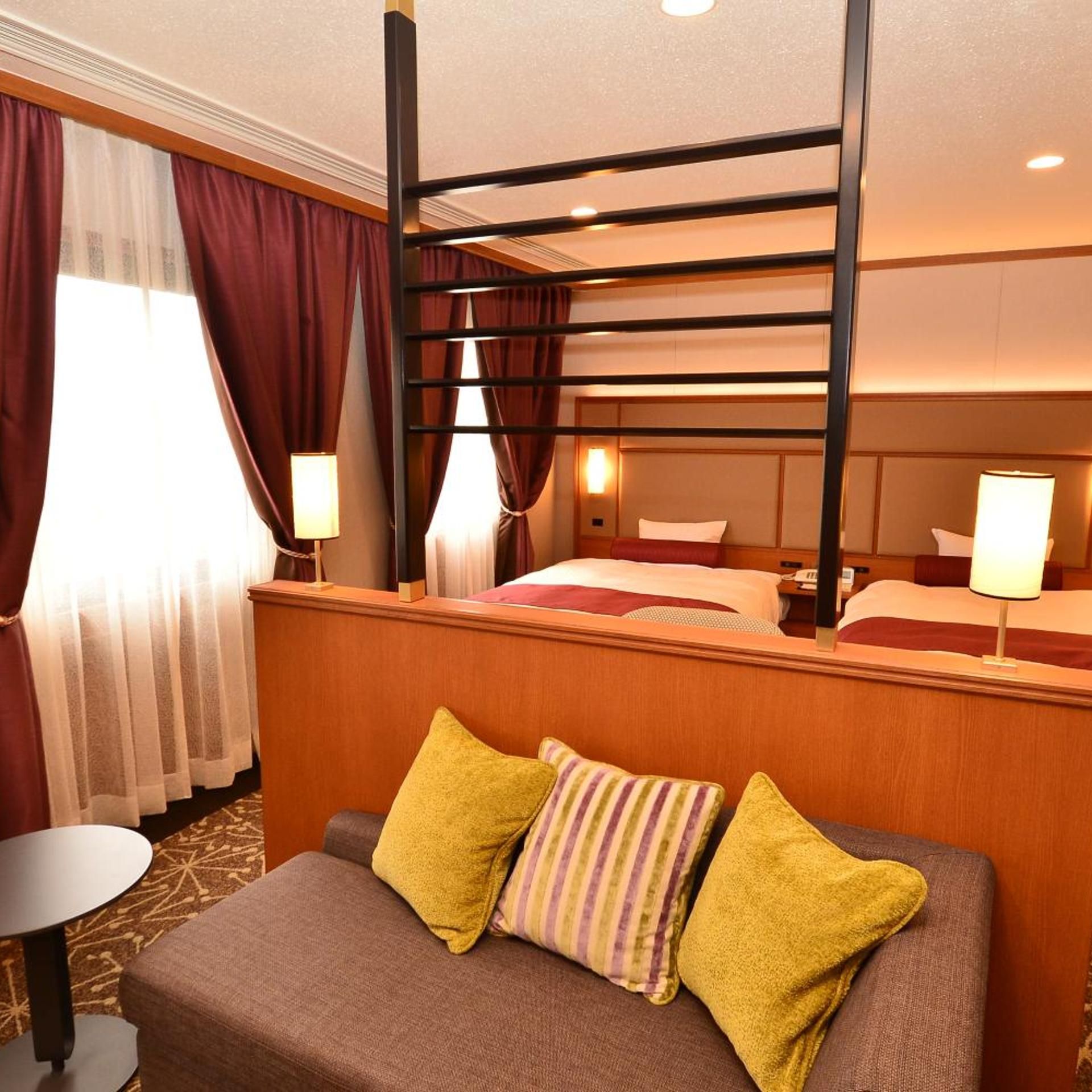 Ein Hotelzimmer mit Etagenbett, einem Einzelbett, einer Couch mit Kissen, einem kleinen Tisch und einer Lampe.