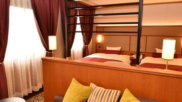Ein Hotelzimmer mit Etagenbett, einem Einzelbett, einer Couch mit Kissen, einem kleinen Tisch und einer Lampe.