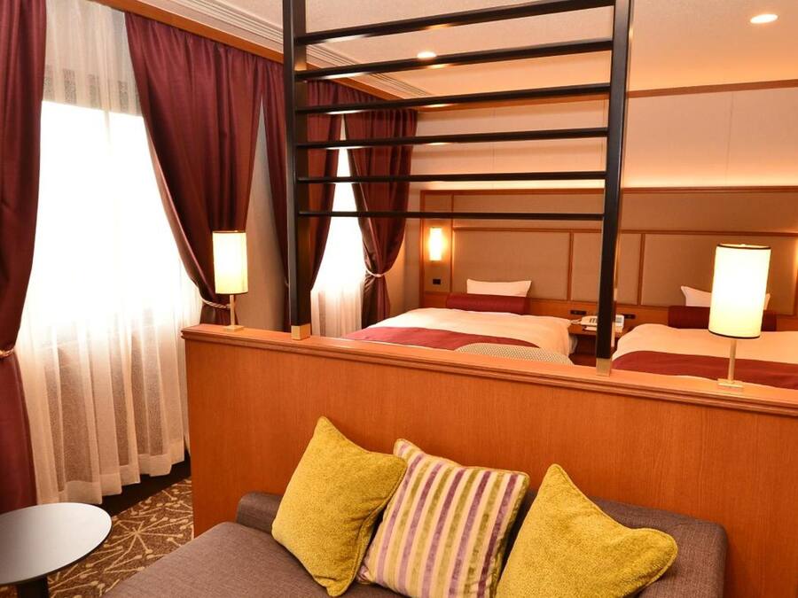 Ein Hotelzimmer mit Etagenbett, einem Einzelbett, einer Couch mit Kissen, einem kleinen Tisch und einer Lampe.