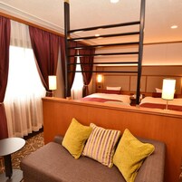 Habitación de hotel con literas, una cama individual, un sofá con almohadas, una mesita y una lámpara.