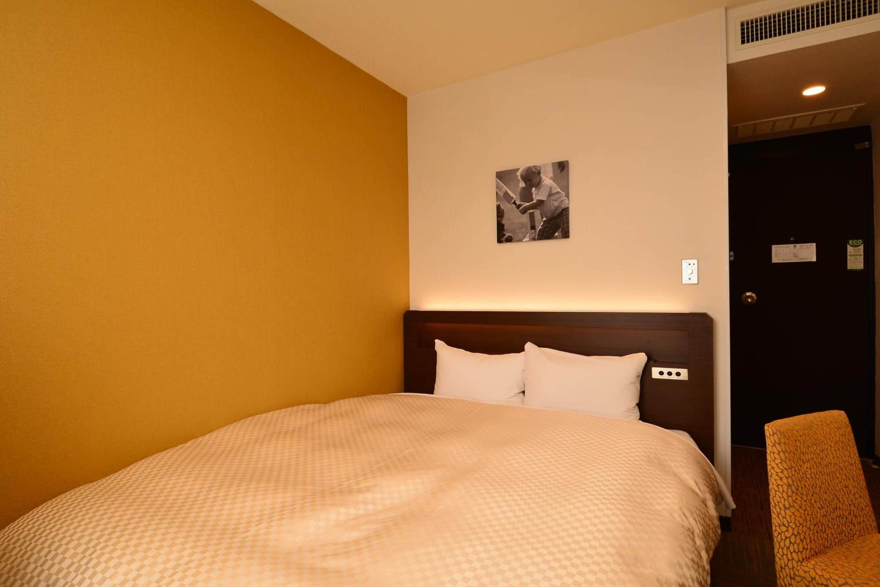 A hotel room with a large bed, a headboard, a wall-mounted picture, and a chair.
